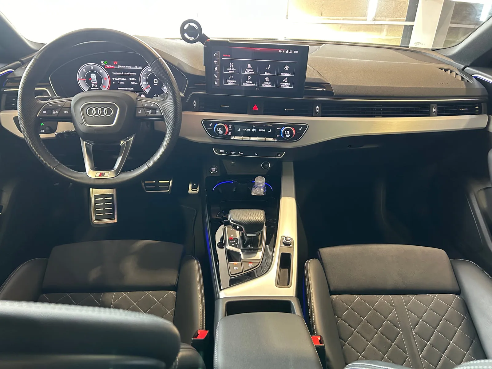 Planche de bord d'une Audi vue de face : volant à anneaux, écran tactile, sièges noirs à surpiqûres en losanges
