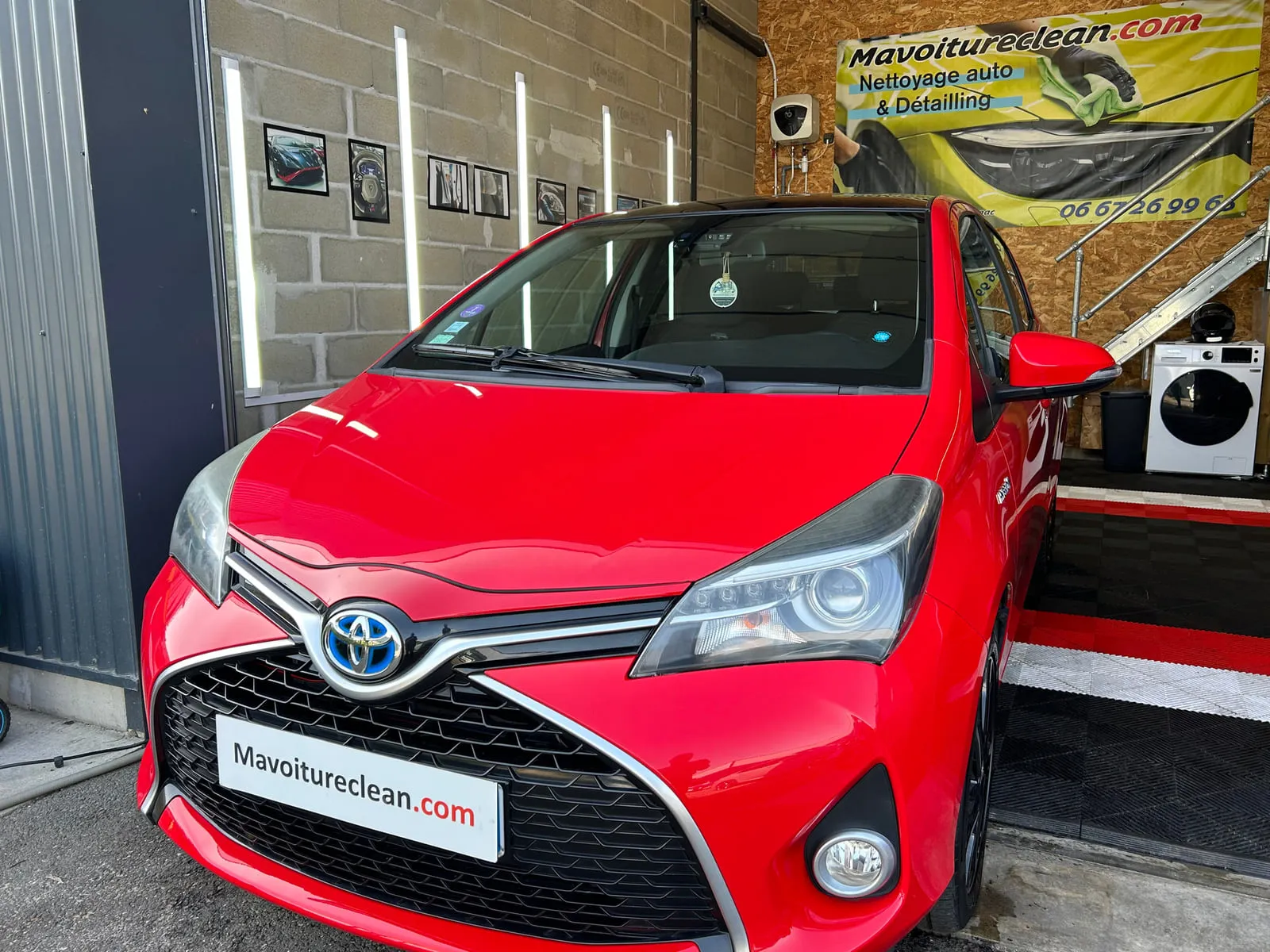 Toyota rouge vue de face à l'entrée de l'atelier, logo à fond bleu, bannière Mavoitureclean.com au fond
